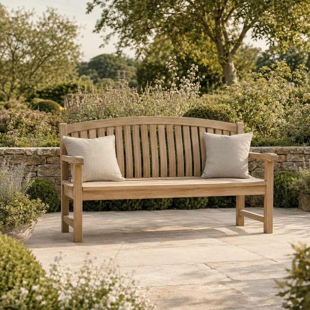 Elegant wooden garden bench with cream cushions on a stone patio surrounded by flowers and greenery – Verdant Lounge UK