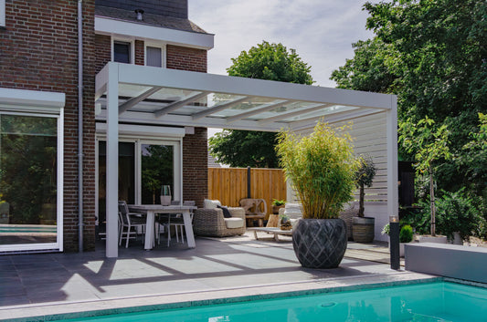 White Pinela Glass Pergola installed beside a modern house with outdoor dining furniture and swimming pool